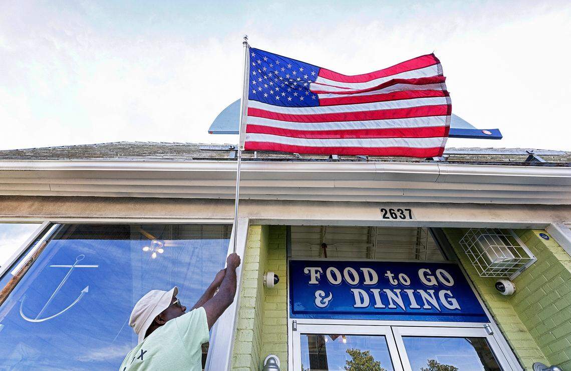Ricky Moore, chef and owner of Saltbox Seafood Joint, adjusts an American flag at the restaurant’s entrance on Wednesday, Nov. 16, 2022, in Durham, N.C. Moore is The News & Observer’s 2022 Tar Heel of the Year.