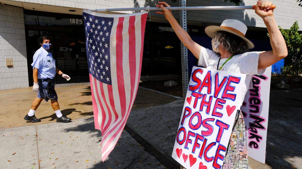 Erica Koesler of Los Angeles demonstrates outside outside a USPS post office as a postal worker walks by in the background, Saturday, Aug. 15, 2020, in the Los Feliz section of Los Angeles. The USPS has warned states coast to coast that it cannot guarantee all ballots cast by mail for the November election will arrive in time to be counted, even if mailed by state deadlines, raising the possibility that millions of voters could be disenfranchised.