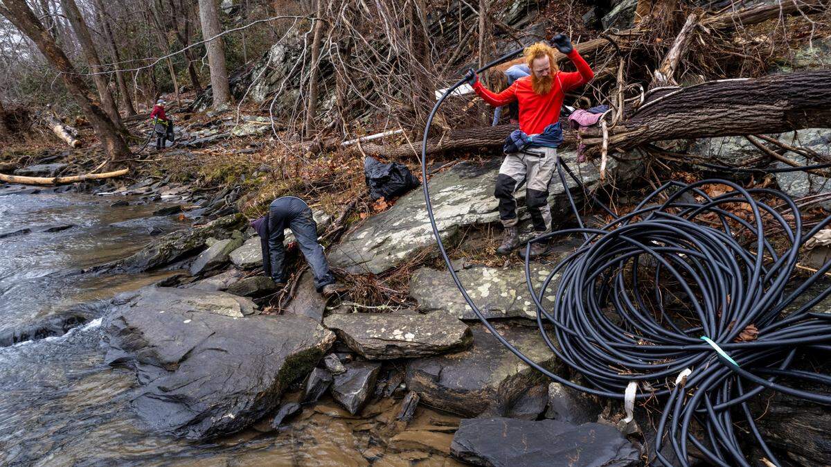 Jordan Clark-Brown, right, and Katie Miller with Mountain True clean trash and debris along the French Broad River near Marshall on Monday, Jan. 27, 2025. Using private donations, Mountain True launched a pilot program aimed at removing trash out of North Carolina rivers following catastrophic flooding from the remnants of Hurricane Helene last year.