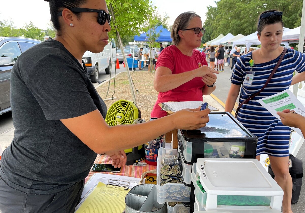 Chapel Hill Farmers’ Market Assistant Manager Tenita Solanto (left) and other staff members answer questions while handing out Double Bucks tokens to a customer at the South Estes Drive market on Tuesday, July 30, 2024.