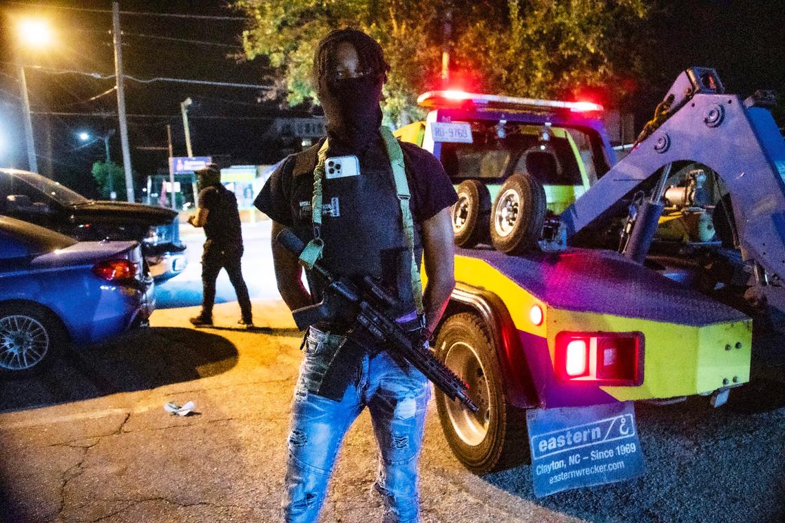 A man who did not want to be identified by stands guard on Peace Street near Glenwood Avenue as tow trucks remove unattended vehicles in a parking lot shortly before 4 a.m. near the Glenwood South district on Friday, July 21, 2023.