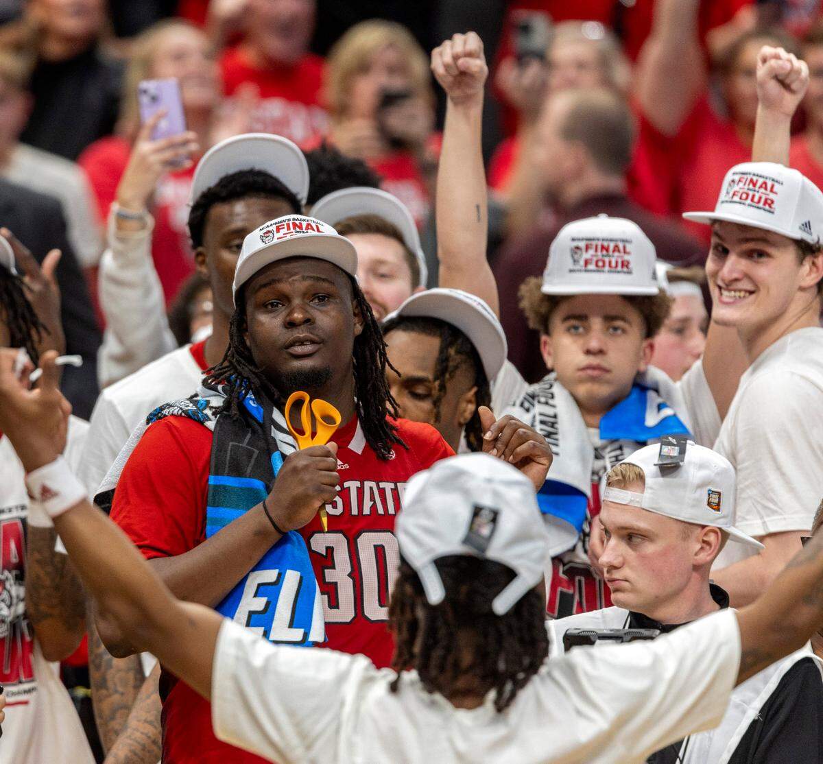 N.C. State’s D.J. Burns Jr. (30) is handed the scissors for his turn to cut down the net, celebrating the Wolfpack’s 76-64 victory over Duke in the NCAA South Regional on Sunday, March 31, 2024 at the American Airlines Center in Dallas, Texas
