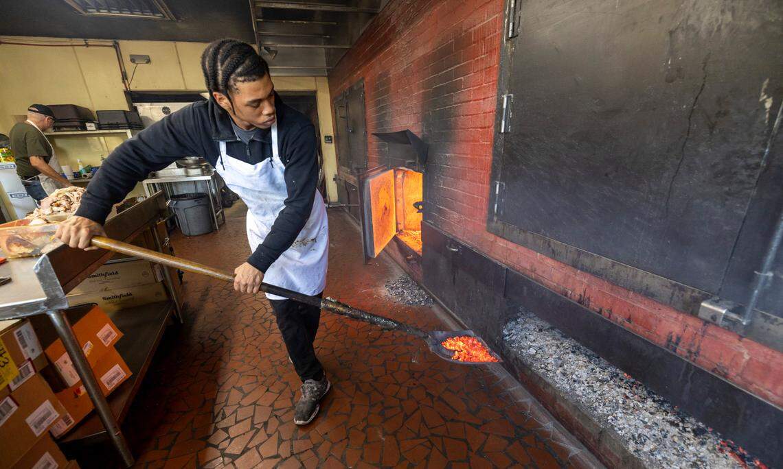 Nkosi Barnes, places hardwood coals beneath the pork shoulders cooking at Lexington Barbecue on Tuesday, October 10, 2023 in Lexington, N.C.