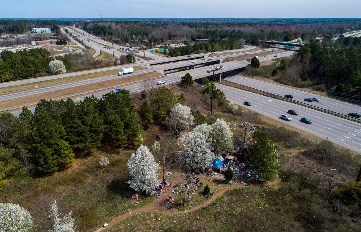 An aerial view of a camp between Interstate 540 and an exit ramp to Capital Boulevard that is littered with trash and debris. The NCDOT has received numerous complaints about the site.