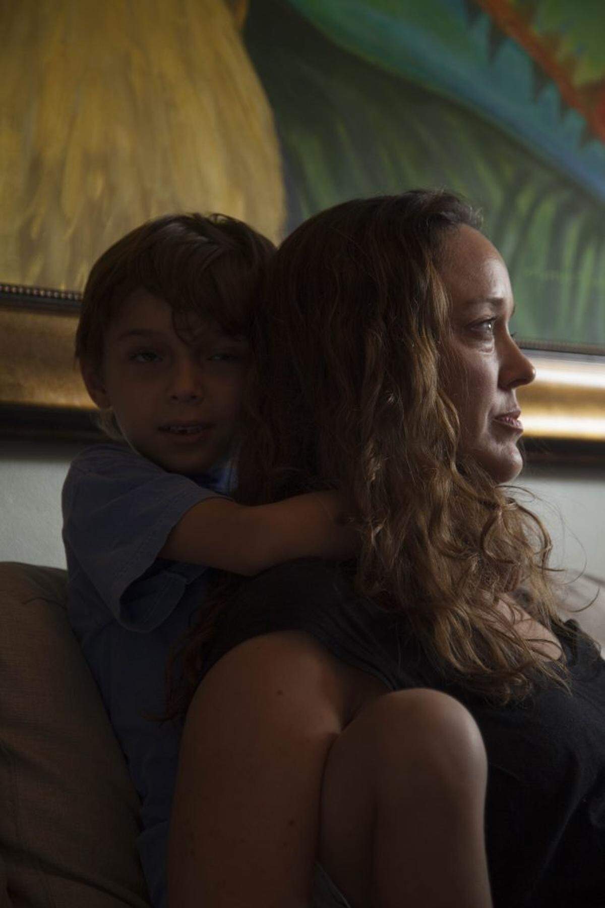 Misty Hedspeth chats with the family while one of her sons clings to her back.