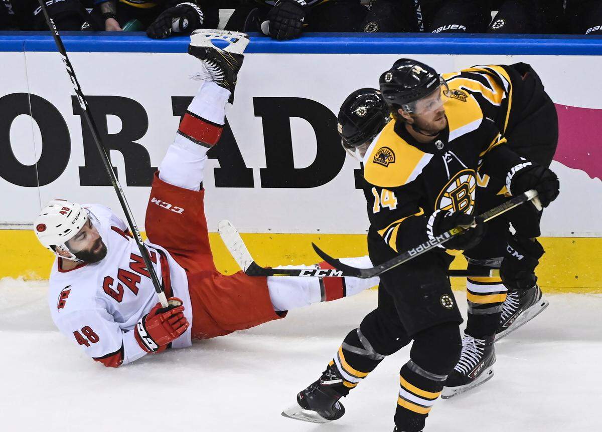 Carolina Hurricanes left wing Jordan Martinook (48) gets hit to the ice against Boston Bruins defenceman Brandon Carlo (25) as Bruins right wing Chris Wagner (14) looks up ice during the first period of an NHL Eastern Conference Stanley Cup playoff hockey game in Toronto, Ontario, on Wednesday, Aug. 19, 2020. (Nathan Denette/The Canadian Press via AP)
