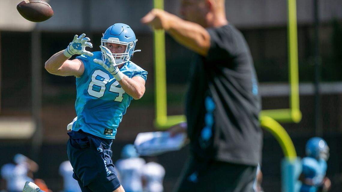 North Carolina tight end Garrett Walston (84) pulls in a pass from quarterback Sam Howell, as offensive coordinator Phil Longo, right, directs the offense during the Tar Heels’ first day of practice on Thursday, August 5, 2021 in Chapel Hill N.C.