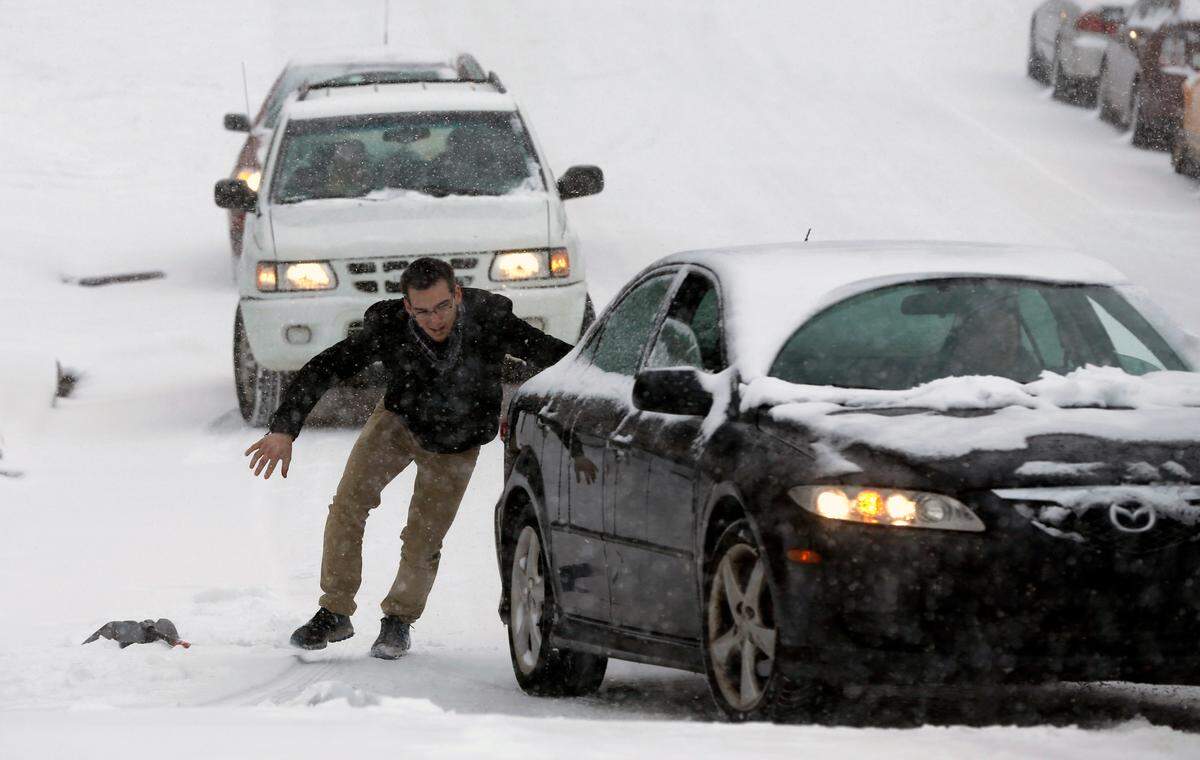 Robert Moss, left, and Isaac Granick (behind car) help Dan Schneider navigate his car up W. Hargett St. in the snow in Raleigh, Wednesday, February 12, 2014.