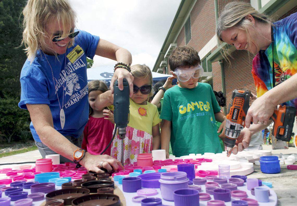 Volunteer Maureen Bizyak, left, helps Emma Grace Risinger as art teacher Dawn Wade helps Michael Montgomery, both first-graders, screw recycled bottle caps onto a giant butterfly in this 2013 Earth Day event organized by the PTA at Lacy Elementary School in Raleigh. Many Wake County schools have restricted visitor access during the COVID pandemic.