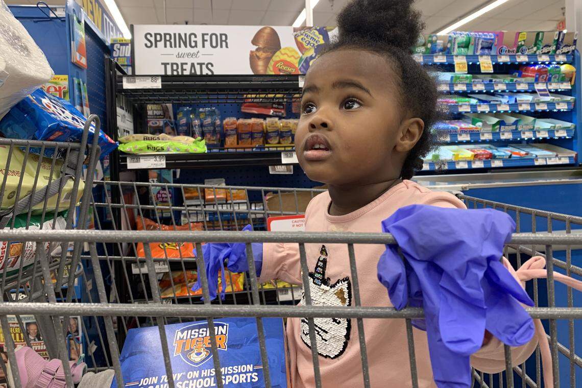 Two-year-old Charlee Sanders wears s a pair of latex gloves while riding in a shopping cart at a Food Lion in Raleigh, Thursday, March 26, 2020. Daily life and tasks as simple as grocery shopping have changed drastically in the midst of the Coronavirus pandemic.