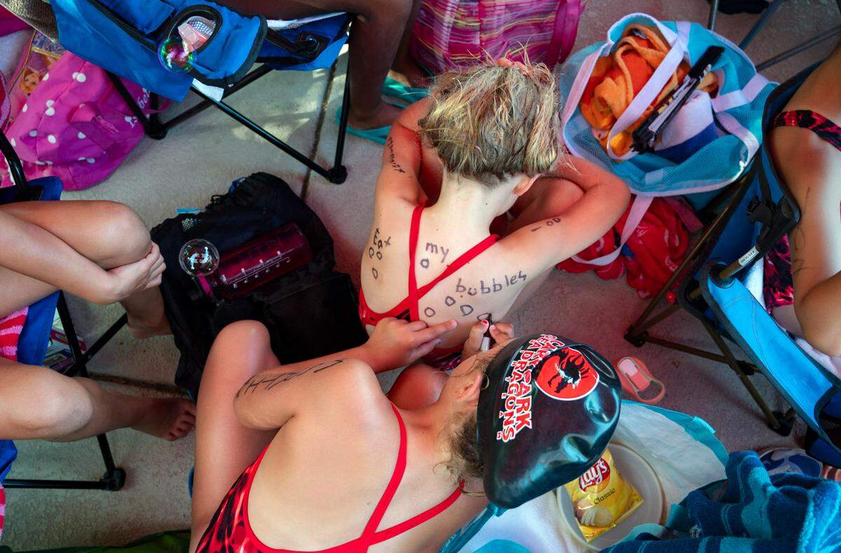 Lila Martin and June Kalberkamp show their spirit at the swim meet by drawing bubbles on their back at Cary Park Swim Club on Tuesday, June 25, 2024. Before the meet the team builds up energy using temporary sea dragon tattoos and putting glitter on their faces.