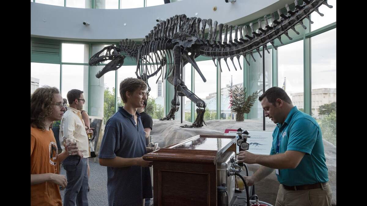 Jason Faulkner of White Street Brewing Co. serves samples to Natural Selections guests in front of the iconic Acrocanthosaurus at the NC Museum of Natural Sciences in 2016.