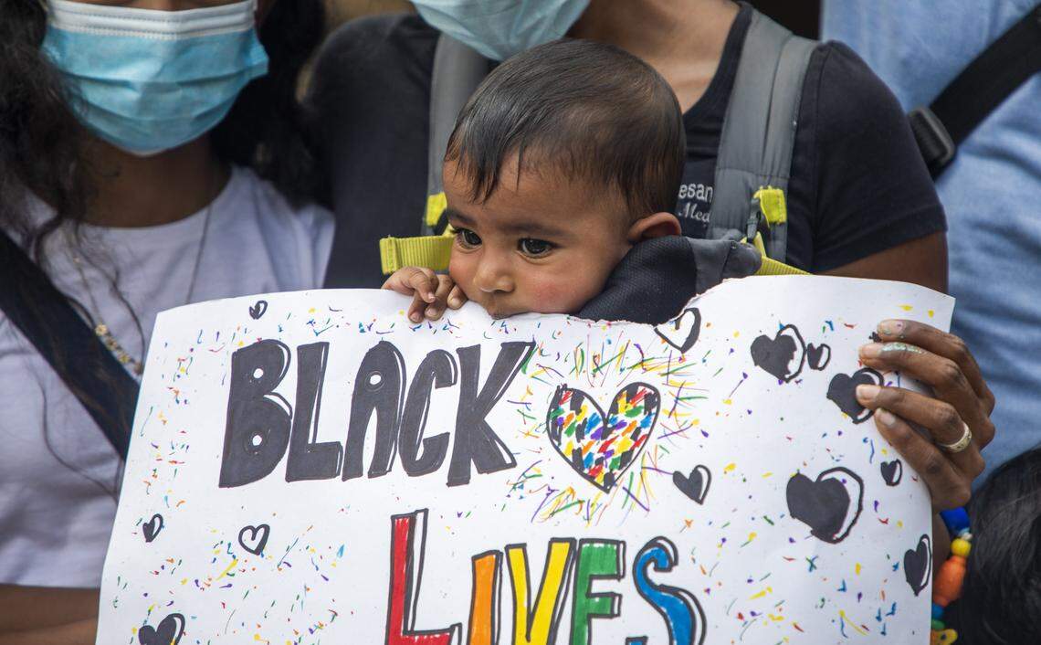 Sajana Natesan-Torres munches on a sign while her mom Sree Natesan, an emergency room doctor at Duke University Hospital, stands for photos during the Triangle Health Care Workers for Black Lives march, that brought hundreds of healthcare workers together to protest in the wake of the death of George Floyd, lead the crowd in chanting as they fill Foster Street on their way to CCB Plaza, on Saturday, Jun. 6, 2020, in Durham, N.C.