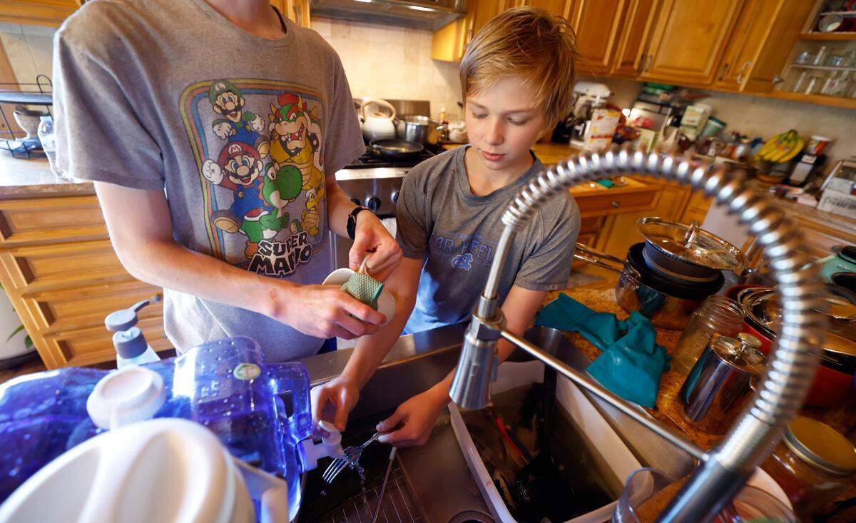 Evan Bloemendaal, 17, washes dishes with his brother Paul, 13, with water from a two gallon container in their home in Banner Elk, N.C., Wednesday, Oct. 9, 2024. The Bloemendaal’s power has been restored but there is no estimate on when they will get water back.