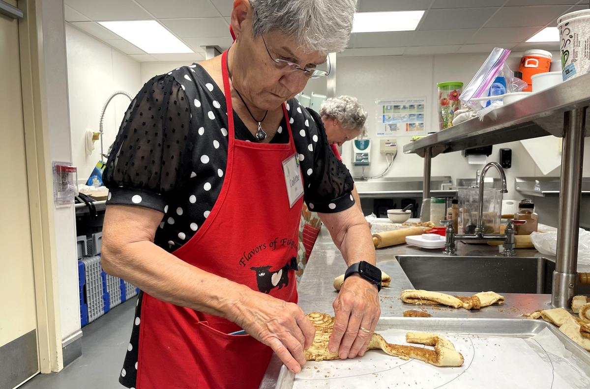 Family House volunteer Colette File layers strips of dough coated in butter, sugar and cinnamon on a sheet pan to form one of four quarters comprising a 3 foot wide cinnamon roll on Friday, Oct. 4, 2024.