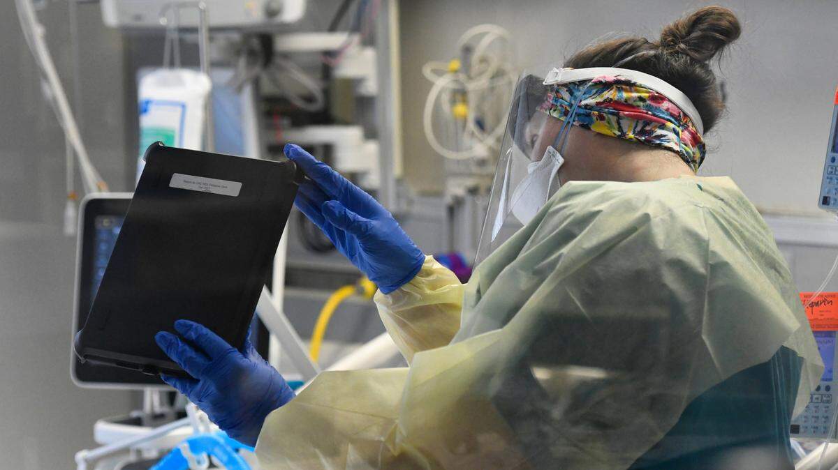 Shannon Costello, RN, a palliative care nurse at UNC Rex Hospital, holds up a tablet so family members can see and talk to a COVID patient via a video FaceTime session Thursday, March 25, 2021.