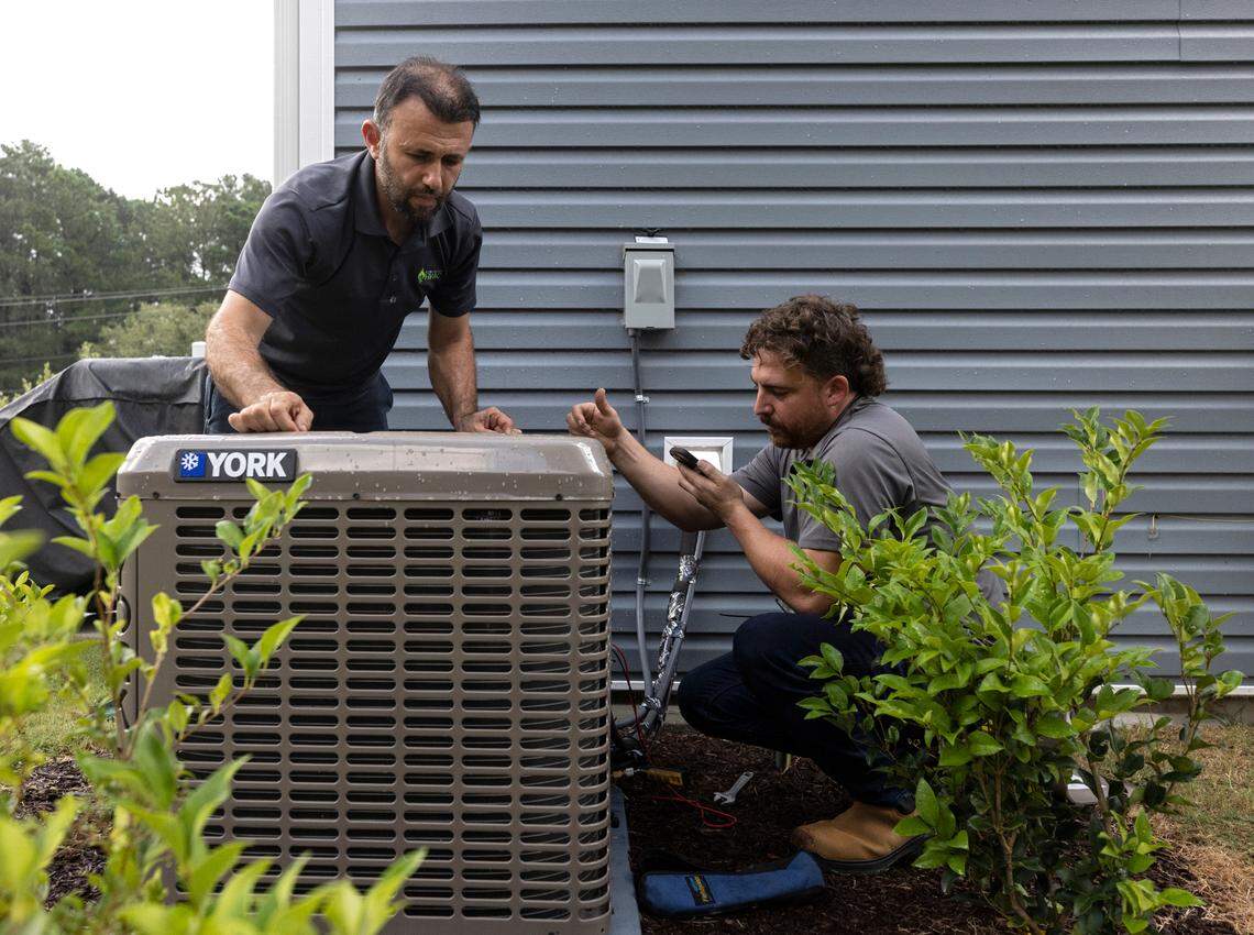 Nihat Yucel and Andrew Ayers of Klimatology HVAC work on an air conditioning unit outside a residence in Raleigh, North Carolina, on Tuesday, Aug. 15, 2023. Experts say AC systems can cool a home to 20 to 30 degrees less than the outdoor temperature.