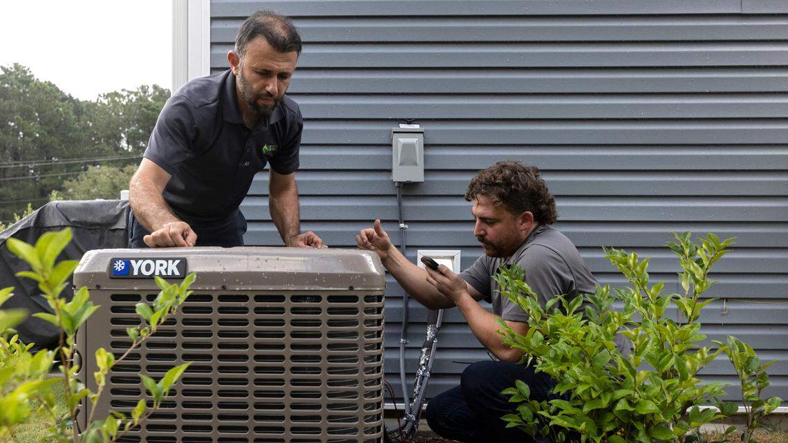 Nihat Yucel and Andrew Ayers of Klimatology HVAC work on an air conditioning unit outside a residence in Raleigh, N.C. on Tuesday, Aug. 15, 2023.