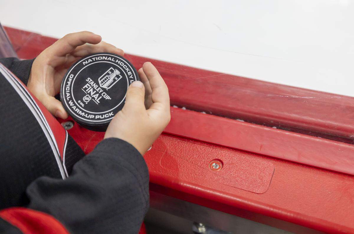 Chase Martinook holds a Stanley Cup commemorative hockey puck, a gift from his father Jordan Martinook (48), as he watches the pre-game skate ahead of Game 1 of the Stanley Cup Finals, on Tuesday, June 2, 2026 at Lenovo Center in Raleigh, N.C.