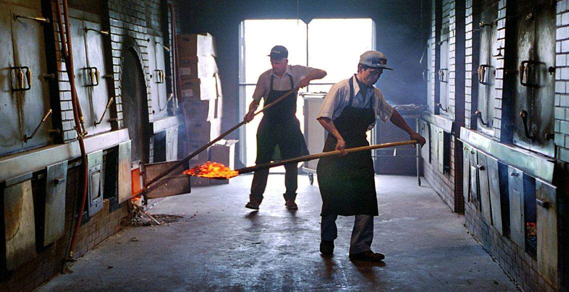 Workers at Stamey’s restaurant in Greensboro shovel coals from a hardwood fire into pits.