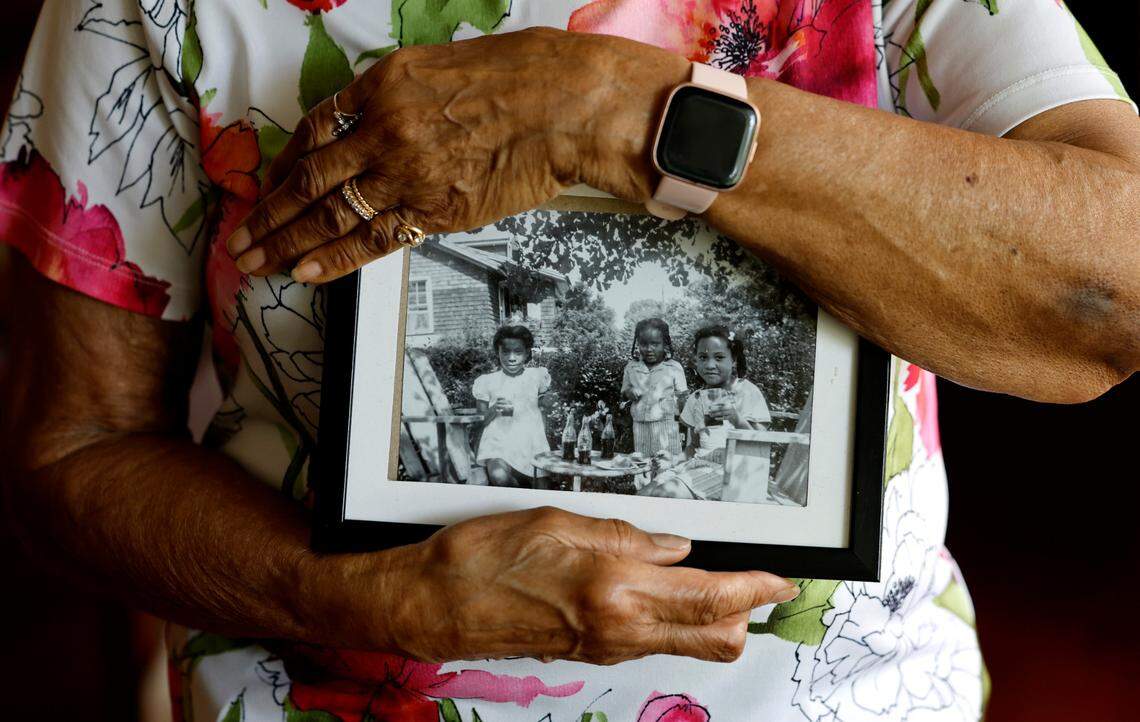Majorie Tucker Keith holds a late 1940s photo of herself, center, and her friends having a tea party outside the home she grew up in in Oberlin Village in Raleigh, N.C.