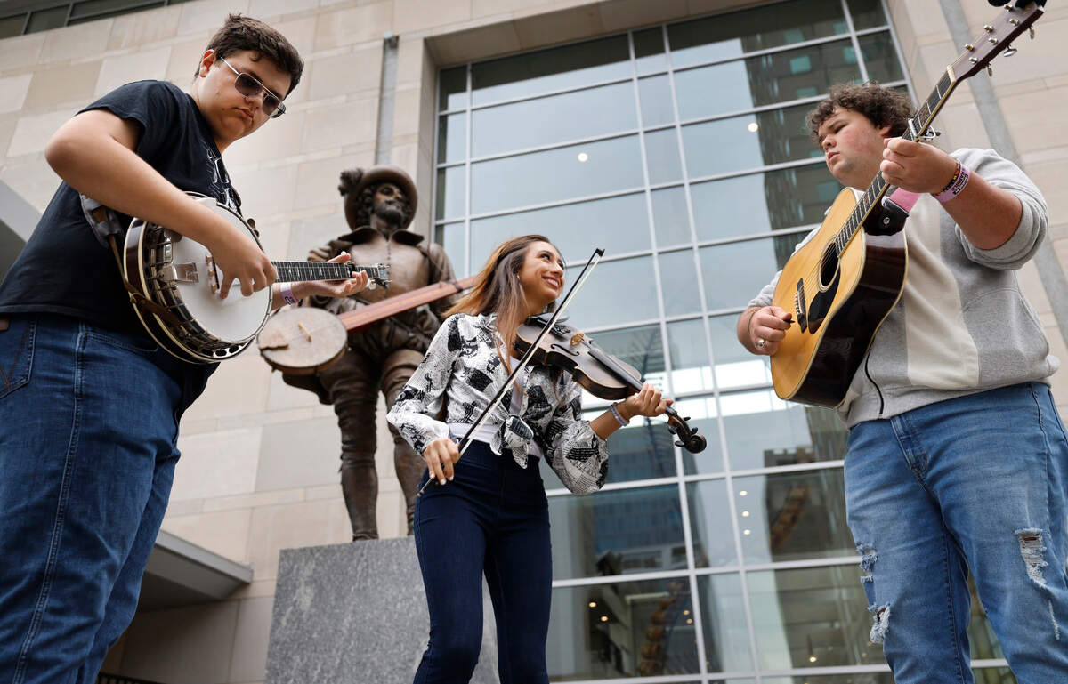 From left, Koltyn West on the banjo, Mary Parker on fiddle and Paul Grace on guitar play in front of the Sir Walter Raleigh statue outside the Raleigh Convention Center Thursday, Sept. 26, 2024. The three are freshman at Bethel University in McKenzie, Tenn. and are in town for IBMA World of Bluegrass. IBMA Bluegrass Live! which includes free concerts on six stages and a street festival in and around Fayetteville Street occurs on Friday and Saturday. This year will be the last year the IBMA holds its event in Raleigh.