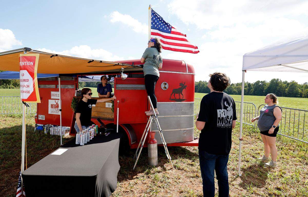 Katie Jenkins, an owner of Red Moose Brewing Company in Pittsboro, sets a flag on their Mobile Moose Kaboose before “Flagstock 2024,” an invite-only concert featuring country musicians Big & Rich and Lee Greenwood, among others, at a location in Chapel Hill, N.C., Monday, Sept. 2, 2024. Flagstock started after a GoFundMe raised over $515,000 for a “rager” for UNC-Chapel Hill fraternity brothers who held up the American flag during an April campus protest.