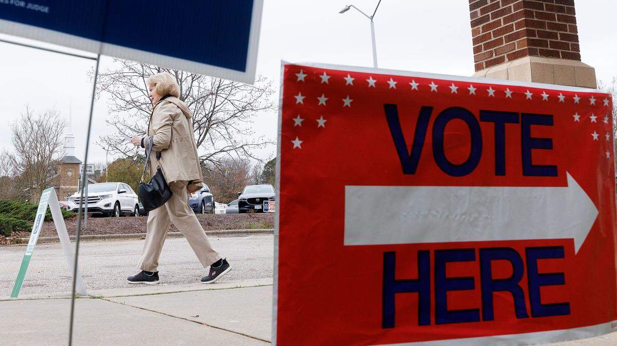 A person walks by voting and campaign signs outside of Aversboro Elementary School on Tuesday, March 5, 2024, in Garner, N.C.