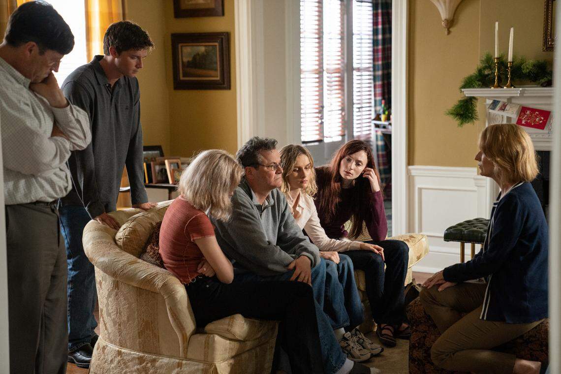 From the HBO limited series “The Staircase”: (standing, L-R) Tim Guinee, Patrick Schwarzenegger, (on sofa, L-R) Odessa Young, Olivia DeJonge, Colin Firth, Sophie Turner and (far right) Rosemarie Dewitt.