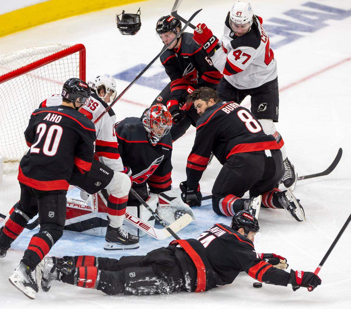 Carolina Hurricanes defenseman Jaccob Slavin (74) covers the puck, as teammate Brent Burns (8) looses his helmet as they assist Hurricanes goalie Frederik Andersen (31) on a scoring attempt by the New Jersey Devils in the second period during game two of their Stanley Cup playoff series on Tuesday, April 22, 2025 at Lenovo Center in Raleigh, N.C.