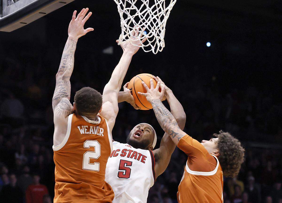 N.C. State’s Tre Holloman is fouled as he drives against Texas’ Chendall Weaver and Jordan Pope with less than a minute remaining in the Wolfpack’s 68-66 loss in the NCAA First Four on Tuesday, March 17, 2026, at the University of Dayton Arena in Dayton, Ohio. 