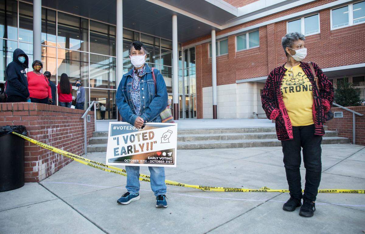 Faye Mitchell, left, and Denise Hester, right, wait outside the Turner Law Building at N.C. Central University in Durham, N.C. to cast their votes on the first day of early voting, Thursday, Oct. 15, 2020.