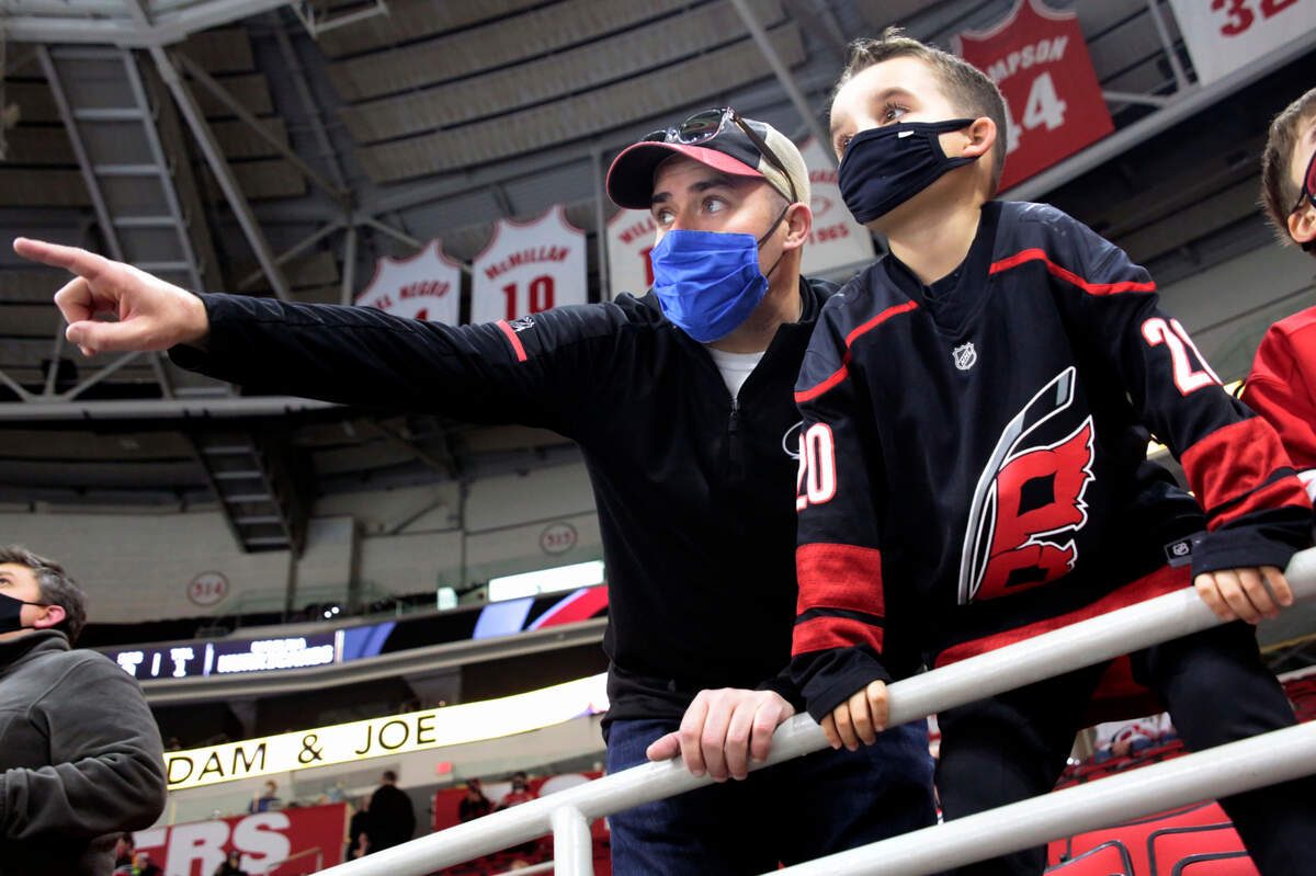 Derek DeYoung, left, points out players to his son Dominic DeYoung as the Carolina Hurricanes warm up before an NHL hockey game against the Detroit Red Wings in Raleigh, N.C., on Thursday, March 4, 2021. It is the first game where a limited number of fans have been allowed in PNC Arena to watch the team.