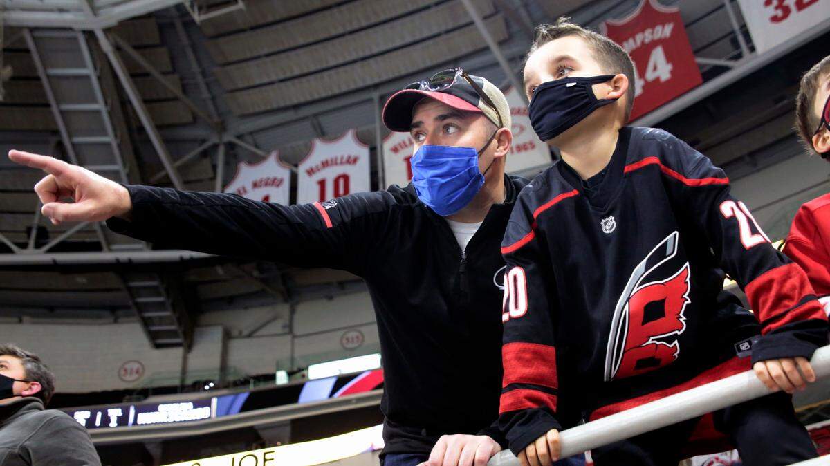 Derek DeYoung, left, points out players to his son Dominic DeYoung as the Carolina Hurricanes warm up before an NHL hockey game against the Detroit Red Wings in Raleigh, N.C., on Thursday, March 4, 2021. It is the first game where a limited number of fans have been allowed in PNC Arena to watch the team.