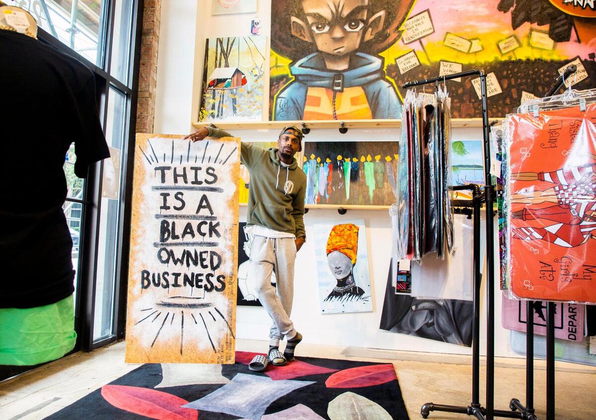 Johnny Hackett stands for a portrait with painted plywood that covered windows downtown during last summer’s protests after the death of George Floyd, inside the Black Friday Market which he opened in December 2019 to sell products and art from small, mostly Black-owned businesses, on Wednesday, Aug 4, 2021, in Raleigh, N.C.