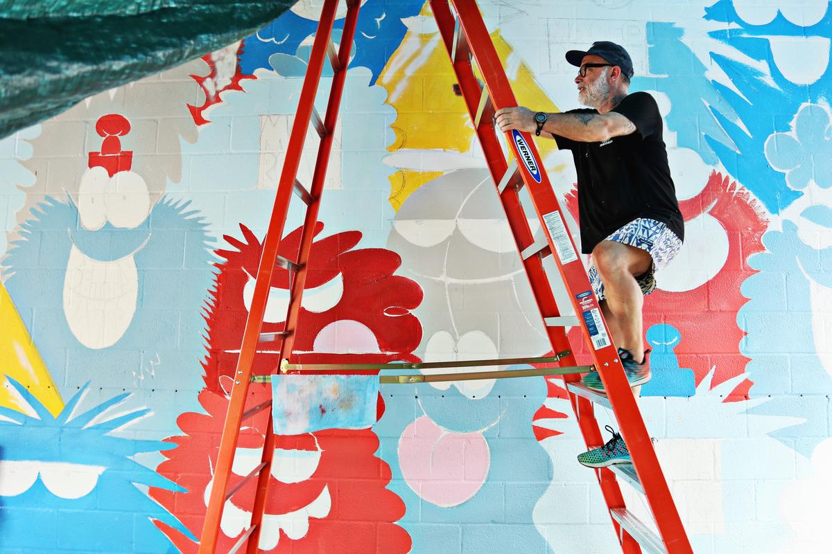 Kevin Lyons, an artist based in Brooklyn, works on his latest mural "Morgan Street Jazz Monsters: A Tribute to the Jazz Giants of North Carolina" on the east wall of Trophy Brewing Co. in Raleigh under a tarp as it rains Wednesday, May 16, 2018.  It replaces a black and white mural Lyons painted on this same wall in 2015.