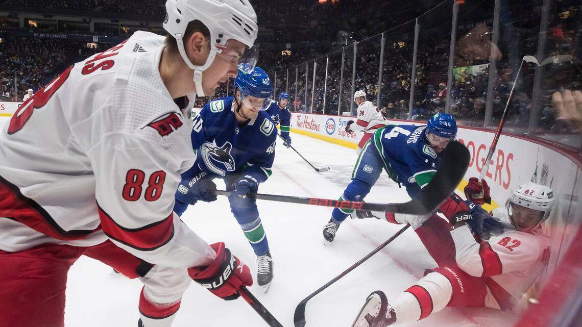 Carolina Hurricanes’ Martin Necas (88), of the Czech Republic, and Jesperi Kotkaniemi (82), of Finland, vie for the puck against Vancouver Canucks’ Kyle Burroughs (44) and Elias Pettersson (40), of Sweden, during the first period of an NHL hockey game in Vancouver, British Columbia, Sunday, Dec. 12, 2021. (Darryl Dyck/The Canadian Press via AP)