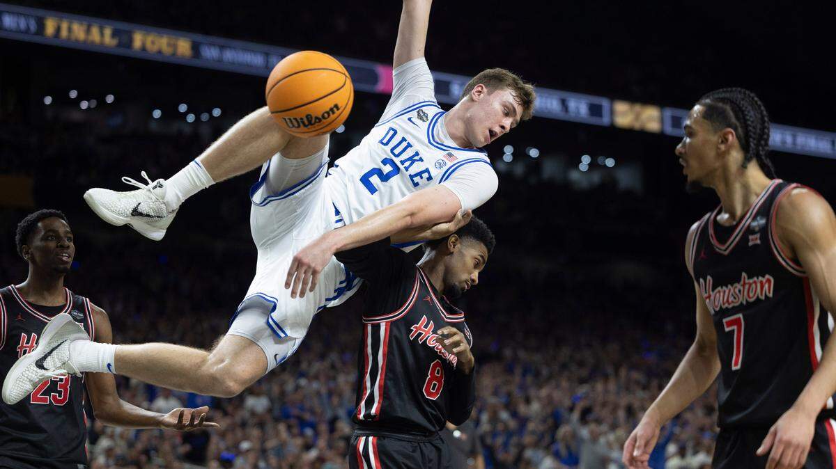 Duke forward Cooper Flagg (2) hangs on the rim above Houston guard Mylik Wilson (8) after a dunk in the first half on Saturday, April 5, 2025 during the NCAA national semi final game at the Alamodome in San Antonio, TX.