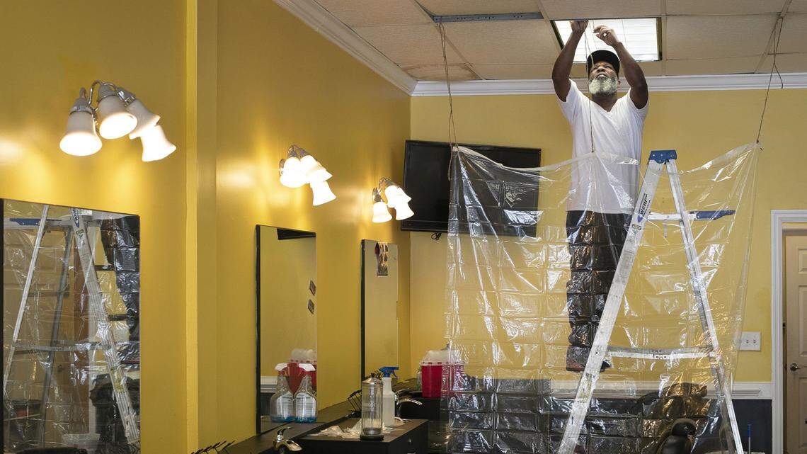 Barber Alex Walton hangs shower curtains between chairs in the Before & After Barbershop on Poole Road as he prepares to open on Friday afternoon, May 22, 2020 in Raleigh, N.C. The shop has been closed since March due to the spread of the COVID-19 virus. ‘It’s inexpensive and it gets the job done’, we’re COVID-19 ready’, Walton said.