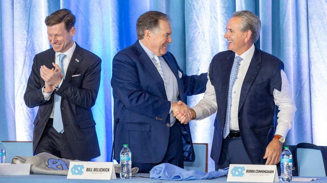 Athletic Director Bubba Cunningham, right, wearing a cutoff jacket, shakes hands with Bill Belichick, center, one of the most accomplished NFL head coaches, as Chancellor Lee Roberts, left, applauds during a press conference at Kenan Stadium on Thursday, Dec. 12, 2024. The event marked Belichick’s official introduction as the new head football coach for UNC-Chapel Hill.