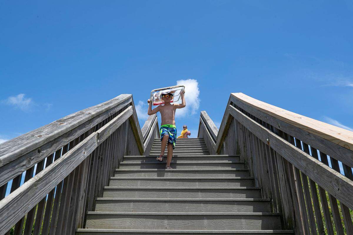 Camden Donai of Pittsburgh, Pa. carries his beach chair down the steps of a beach access point on Tuesday, June 29, 2021 in Nags Head, N.C.