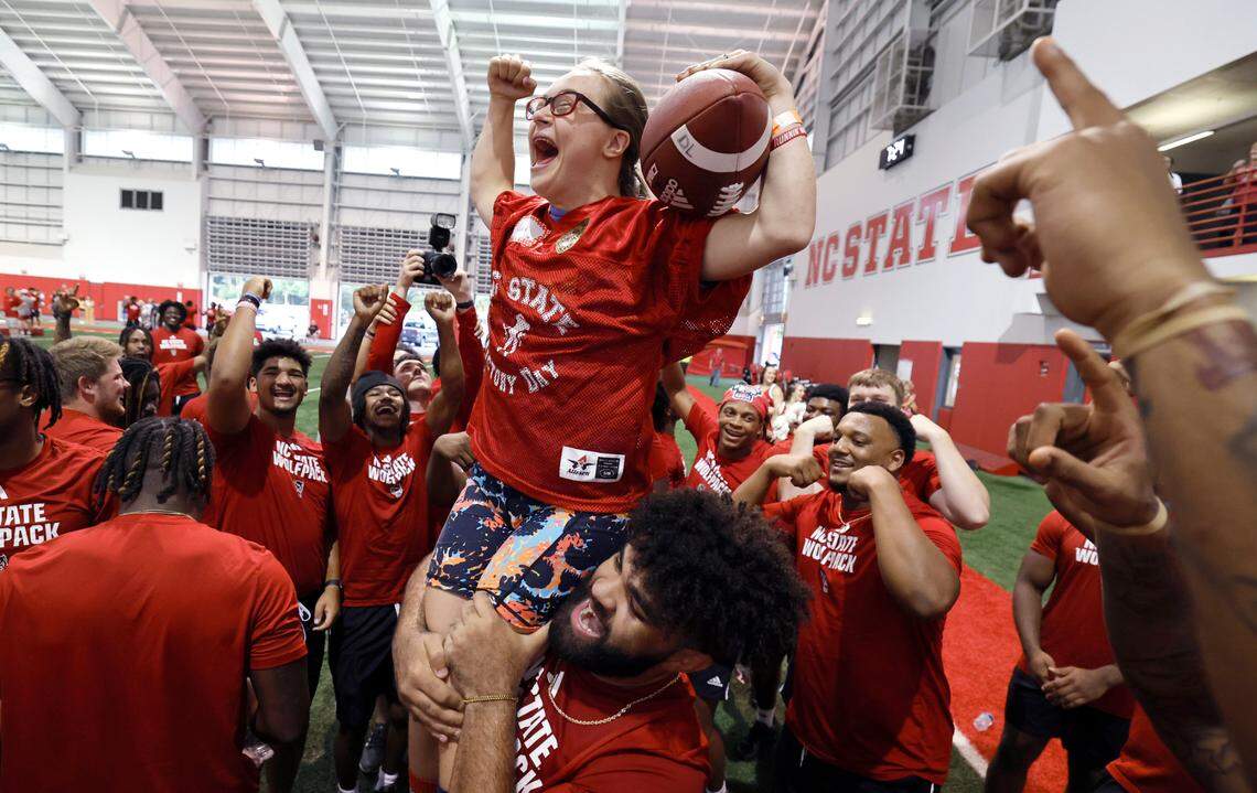 N.C. State offensive lineman Rylan Vann lifts up Gabi Angelini after she scored a touchdown on “Victory Day” at the Close-King Indoor Practice Facility in Raleigh, N.C., Friday, August 4, 2023. On Victory Day Wolfpack football partners with GiGi’s Playhouse Raleigh, a Down Syndrome Achievement Center, to give participants a chance to be a player for the evening. “You guys are a part of our team, you’re part of our family,” said coach Dave Doeren at the start. “Tonight is about you.” Participants were connected with a player and ran drills, tried on uniforms and scored touchdowns. “I was smiling the whole time,” said quarterback Brennan Armstrong. “Like my face hurts because I was smiling so much.”