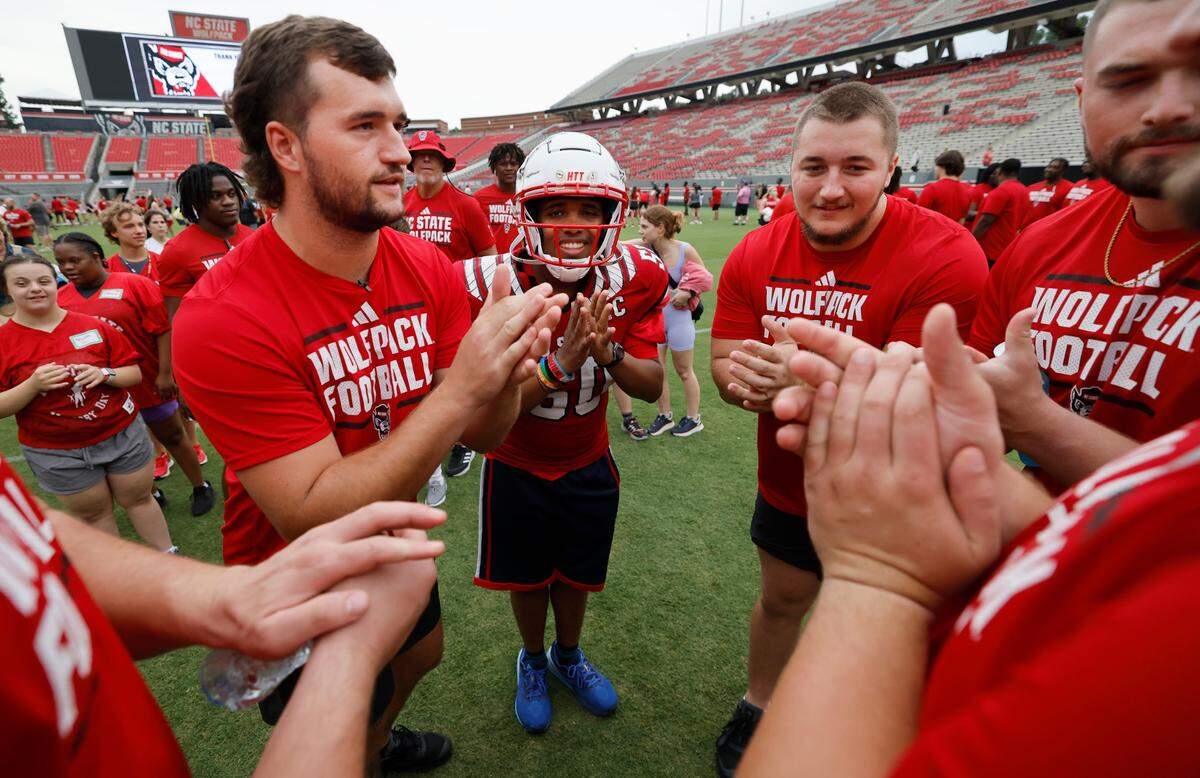 N.C. State quarterback Grayson McCall, left, and members of the offense huddle with William Jennings before running a play during Victory Day at Carter-Finley Stadium in Raleigh, N.C., Friday, August 2, 2024. Victory Day is a partnership between the Wolfpack and GiGi’s Playhouse, a Down Syndrome achievement center in Raleigh.