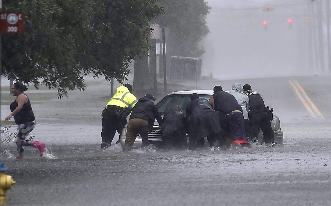 As torrential rain falls Saturday afternoon in Lumberton, NC, police officers help civilians push a stranded motorist out of the flood water near downtown. 