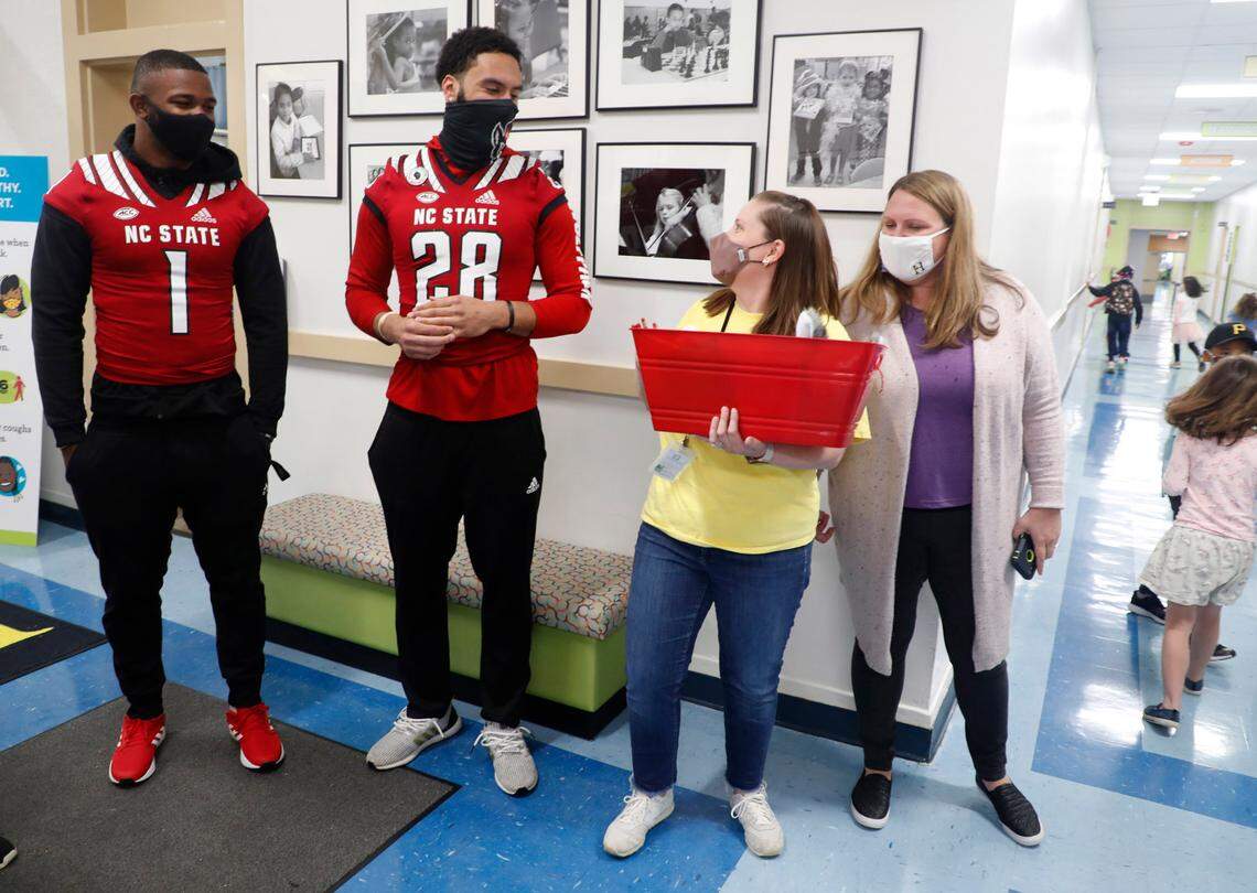 Hunter Magnet Elementary school first grade teacher Andrea Hough, center right, thanks N.C. State football players Isaiah Moore (1), Dylan Parham (28) and Trenton Gill (not in photo) after they delivered a gift basket to Hough in Raleigh, N.C. Friday, May 7, 2021. To the right is Hunter AIG coordinator Angie Parham, Dylan’s mother. To help celebrate teacher appreciation week, players from the Wolfpack football team surprised six teachers from five different schools with gift baskets filled with N.C. State goodies.