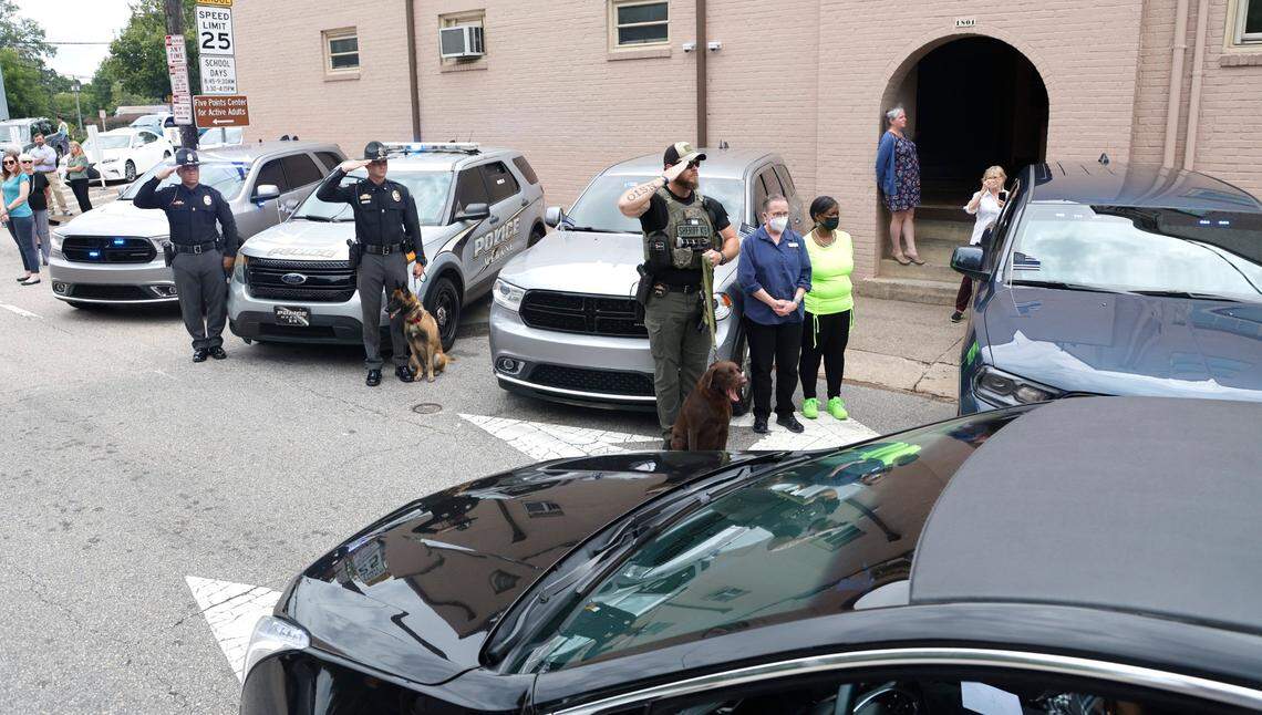 From left, Mebane police officer Russell Suitt, Mebane K9 officer Brandon Coats with his dog Rex and a Lee County K9 officer salute as the procession for slain Wake County Sheriffs Deputy Ned Byrd drives down Glenwood Avenue past the Five Points neighborhood in Raleigh, N.C., Friday, August 19, 2022.