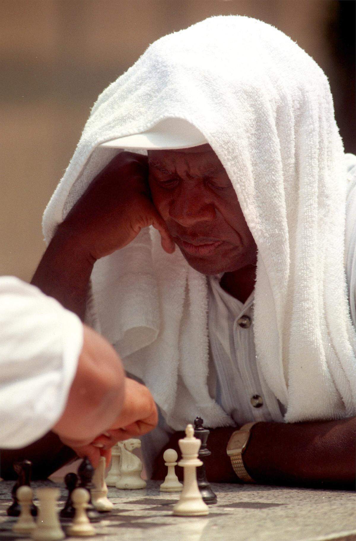 Draped in a cool towel, Sherman Leathers of Raleigh ignores the heat as he plays chess with Jesus Rosales in the Fayetteville pedestrian mall on July 6, 1999. 