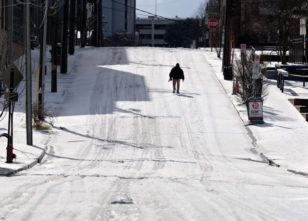 A person walks along Rigsbee Avenue as snow and ice continue to cover some roadways near downtown Durham on Monday, Jan. 26, 2026.