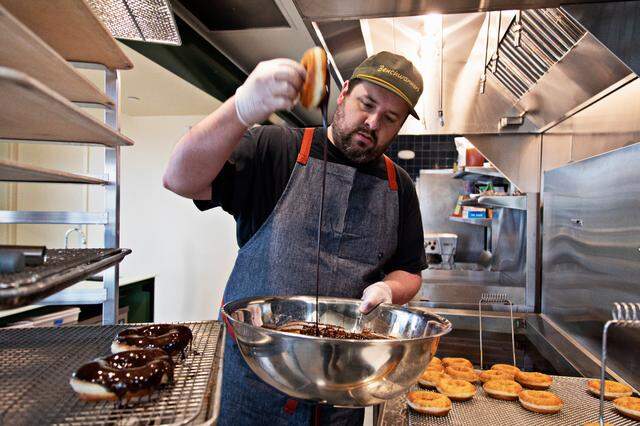 Baker John Knox dips freshly fried donuts into the chocolate glaze he made on Friday, March 18, 2022, at the new Raleigh bakery, Bright Spot Donuts, which will open soon near the Five Points Neighborhood.