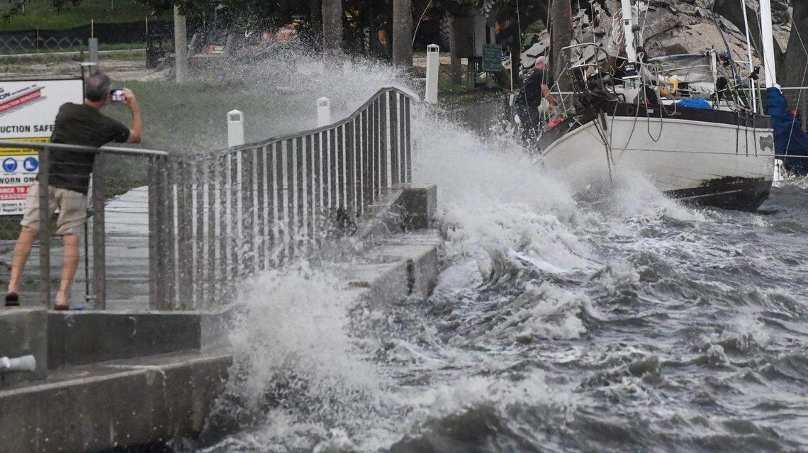 Spectators take photos as two men brave the winds and heavy surf to try and secure a boat along the seawall Thursday, September 26, 2024.